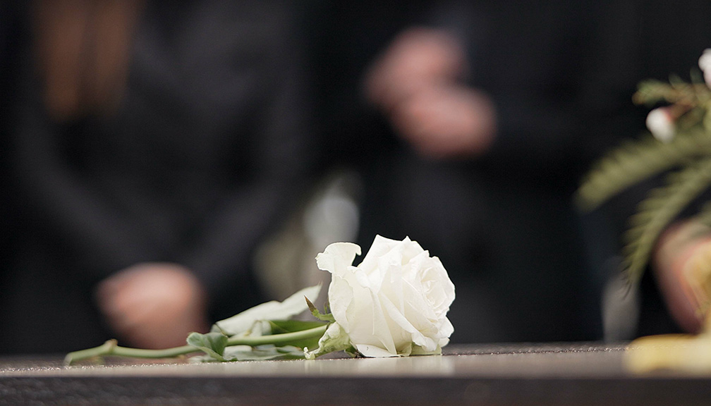 Photo of White Funeral Flower With Mourners in Background